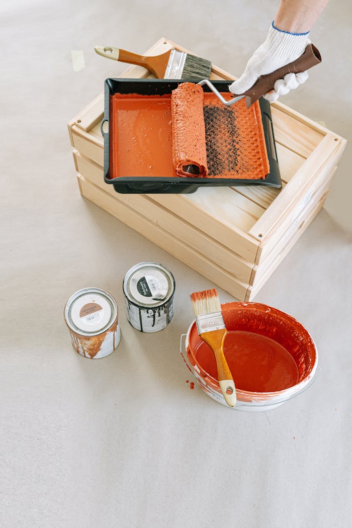 Flat lay of painting supplies on wooden crate, including roller, brushes, and paint cans.